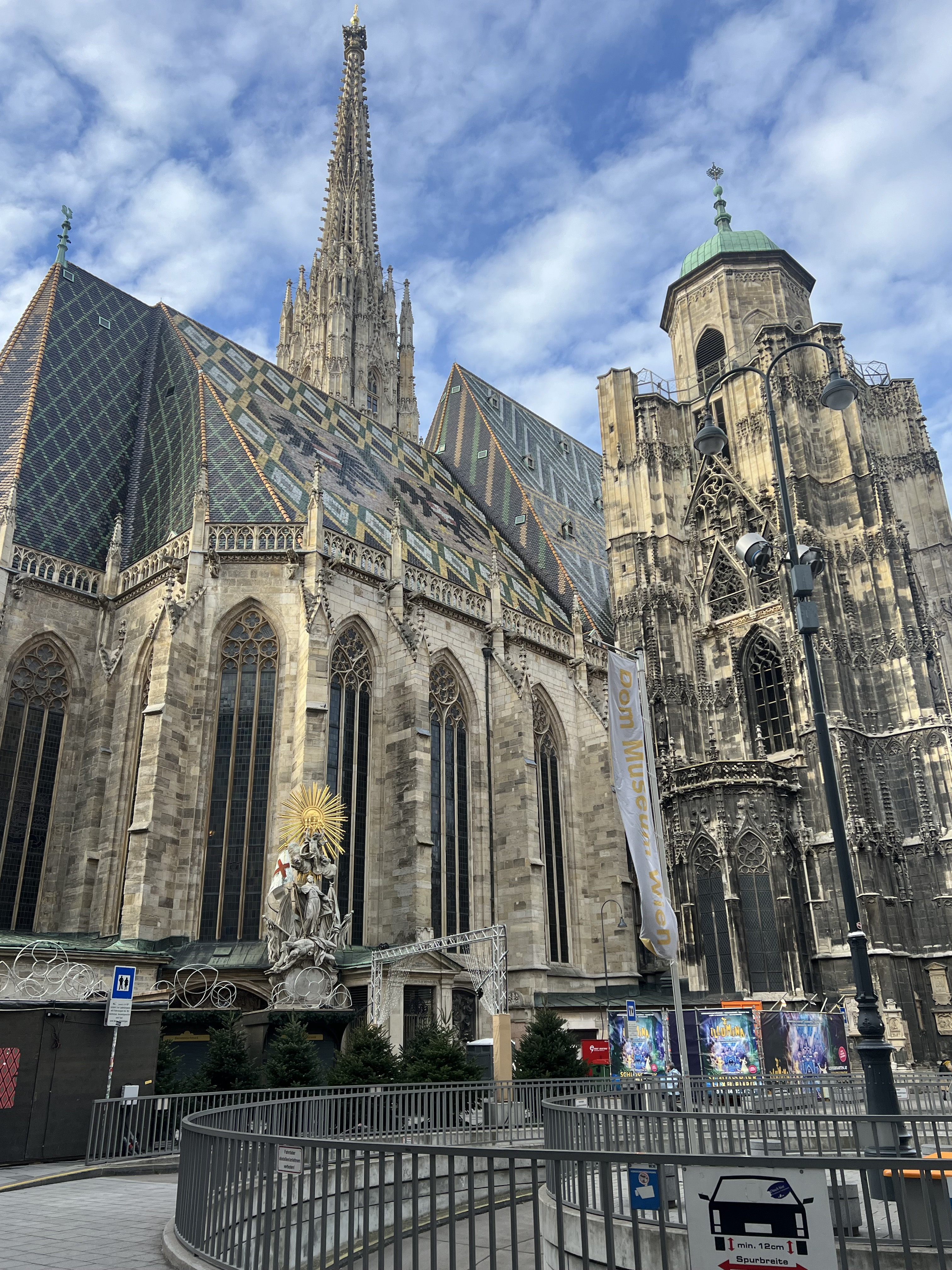 Tall gothic church made of limestone flanked by a blue sky with small white clouds. The roof is adorned with the Austrian coat of arms.
