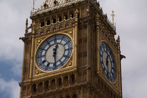 Zoomed in view of the face of Big Ben in London England showing the time as half past 12PM. The sky behind the tower is overcast.