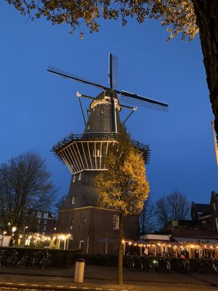 Night time scene of an old wooden windmill with four blades. In the base is a bar with people drinking beer.