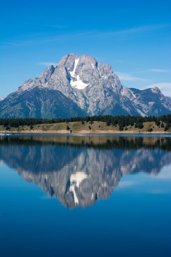 A gray mountain covered with snow surrounded by bright blue sky flawlessly reflected in the lake in the foreground.