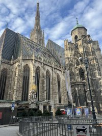 Tall gothic church made of limestone flanked by a blue sky with small white clouds. The roof is adorned with the Austrian coat of arms.