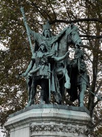 Bronze sculpture of emperor Charlemagne mounted on horseback holding up a staff with his right arm. The statue has a green patina from the weather.