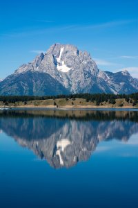 A gray mountain covered with snow surrounded by bright blue sky flawlessly reflected in the lake in the foreground.